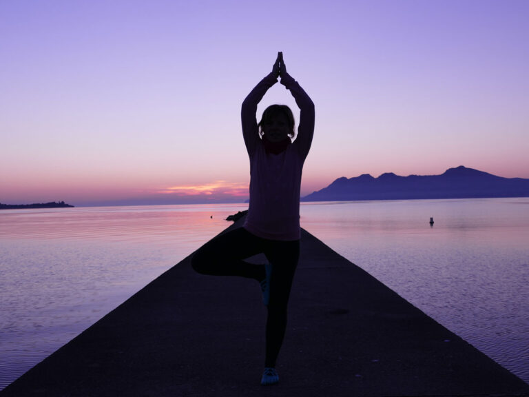 Silhouette beim Yoga auf einem Steg im Sonnenaufgang