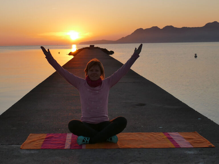 Frau macht Yoga auf Steg bei Sonnenaufgang