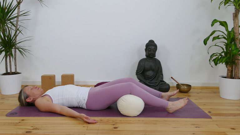Frau entspannt auf Yogamatte mit Kissen unter den Knien